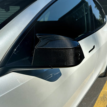 Gloss carbon fiber mirror cover installed on a white Tesla Model Y Juniper, showing the raised bull-horn tip