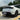 Front three-quarter view of a white Tesla Model Y Juniper featuring Arachnid 2.0 style wheel covers and gloss black Performance style fog light trim covers.